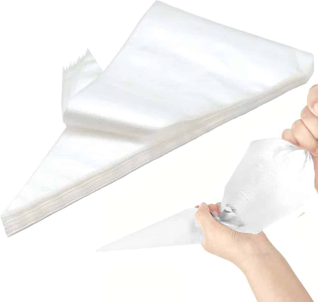 A stack of empty, clear disposable piping bags, with one bag being held and squeezed in a hand—perfect for cake decorating or creating delicate shapes for your favorite meringue cookies recipe.