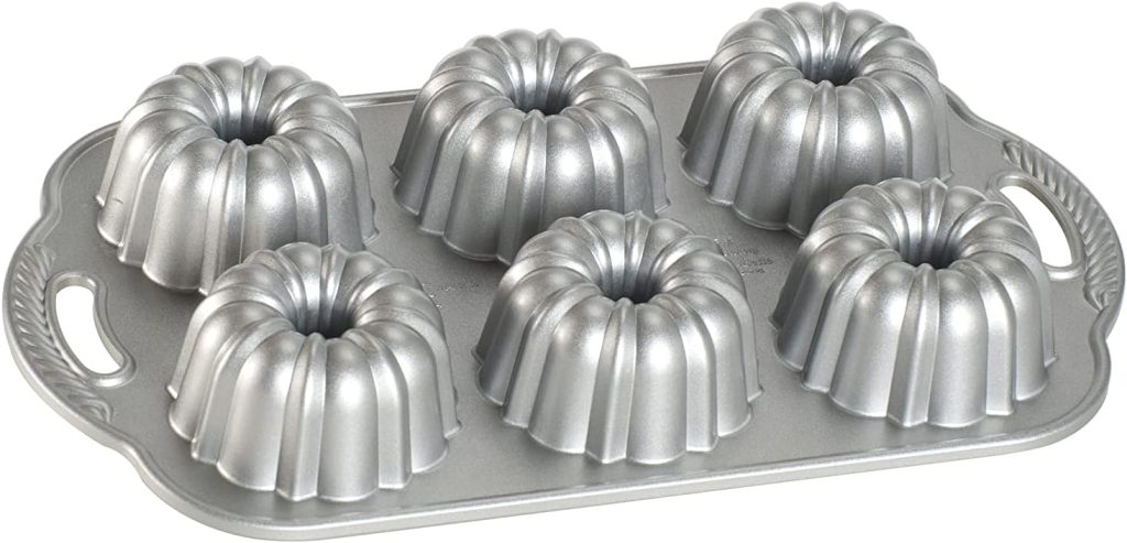 A silver nonstick baking pan with six individual mini Bundt cake molds arranged in two rows, perfect for creating decorative fluted designs on Easter Bundt cakes, and featuring convenient handles on each side.