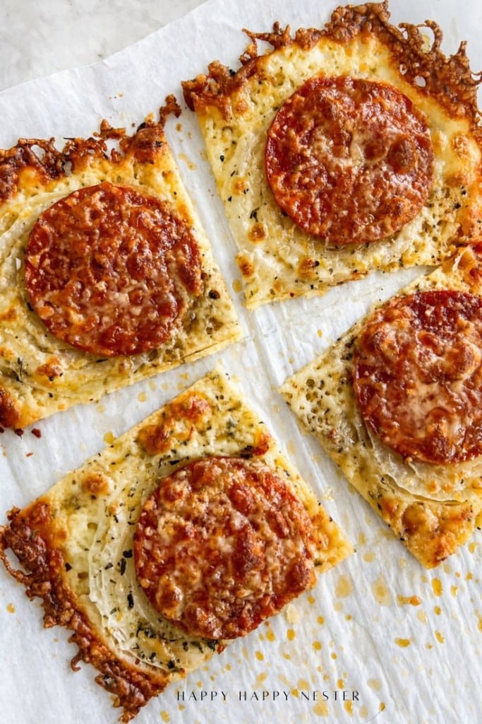 Four square slices of homemade onion ring pizza recipe on parchment paper, each topped with melted cheese, herbs, onions, a slice of pepperoni, and crispy edges where the cheese is browned.