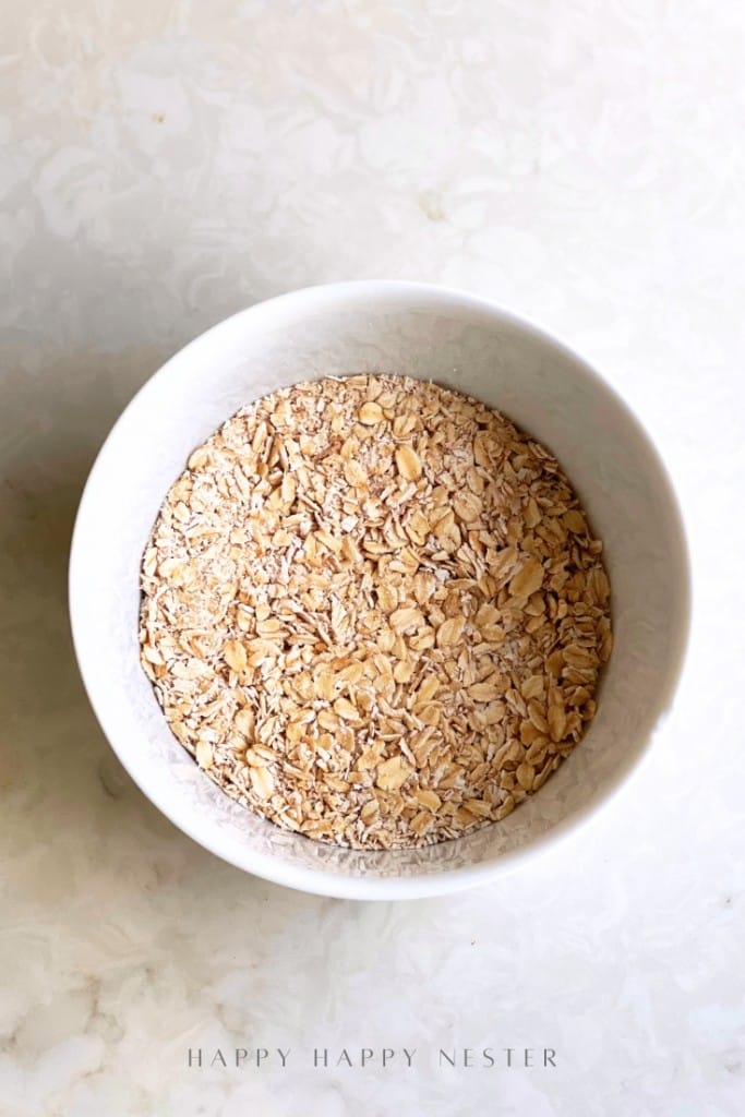 A white bowl filled with dry rolled oats sits on a light-colored, marble-like surface, perfect as the base for an overnight oats recipe with yogurt.