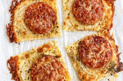 Four square slices of crispy cheese bread topped with pepperoni and grated cheese, arranged on parchment paper with browned, bubbly edges—perfect as a savory side for your favorite onion ring pizza recipe.