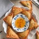A plate of golden, crispy wontons&mdash;made with a classic fried wonton recipe&mdash;arranged around a small bowl of sweet chili dipping sauce, with a bowl of grain salad and napkins in the background.