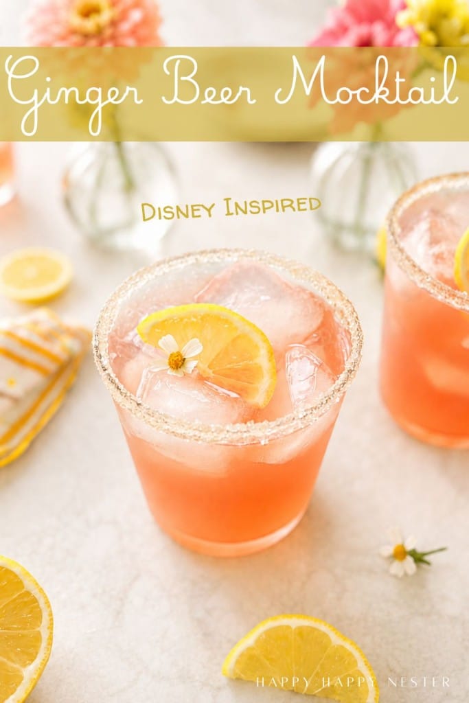 A pink ginger beer mocktail with ice and a lemon slice is served in a sugar-rimmed glass, surrounded by flowers and lemon slices. Text reads: "Ginger Beer Mocktail Recipe, Disney Inspired.