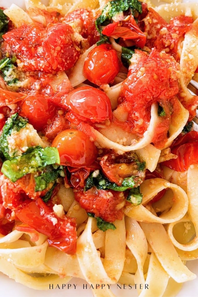 Fettuccine pasta topped with a simple pasta sauce recipe of roasted cherry tomatoes, fresh basil, and grated cheese, all drizzled with olive oil. The dish is vibrant and colorful, with a fresh, homemade appearance.