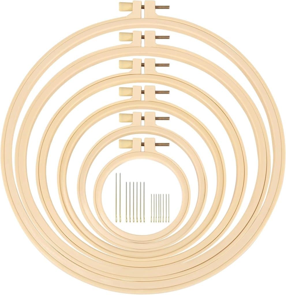 Seven wooden embroidery hoops in graduated sizes are arranged concentrically, echoing the layered look of an oyster shell wreath diy, with a set of ten embroidery needles of varying lengths displayed in the center.