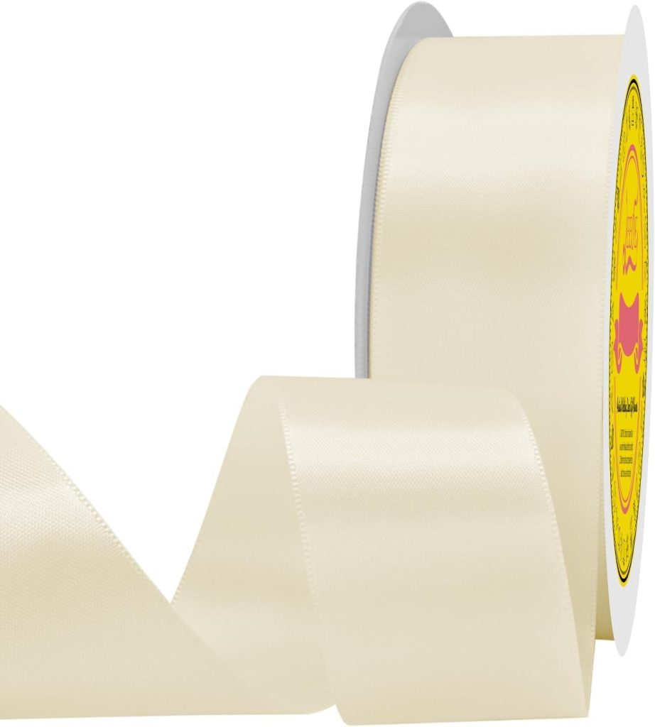 A roll of wide, shiny, ivory-colored satin ribbon with a yellow label on the spool, perfect for oyster shell wreath DIY projects, partially unspooled and gracefully curving in front of a white background.