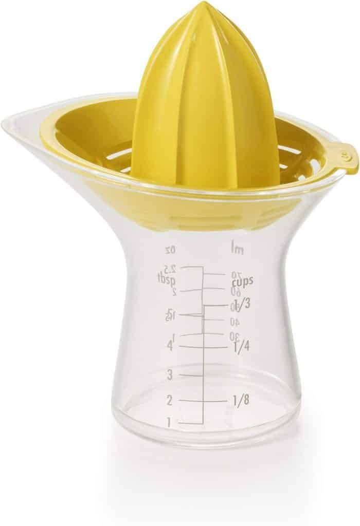 A plastic citrus juicer with a yellow reamer and strainer atop a clear measuring container—perfect for squeezing fresh juice for your favorite lemon aioli sauce recipe, with markings in cups, ounces, tablespoons, and milliliters.