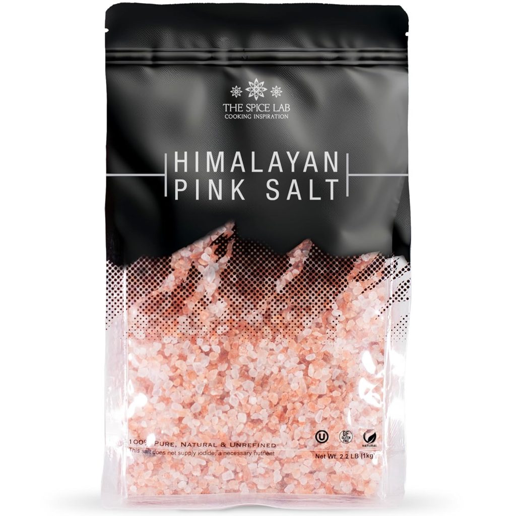 A bag labeled "Himalayan Pink Salt" from The Spice Lab, filled with coarse pink salt crystals in a clear and black resealable package. Perfect for enhancing a lemon aioli sauce recipe. The net weight is 2 lbs (907g).