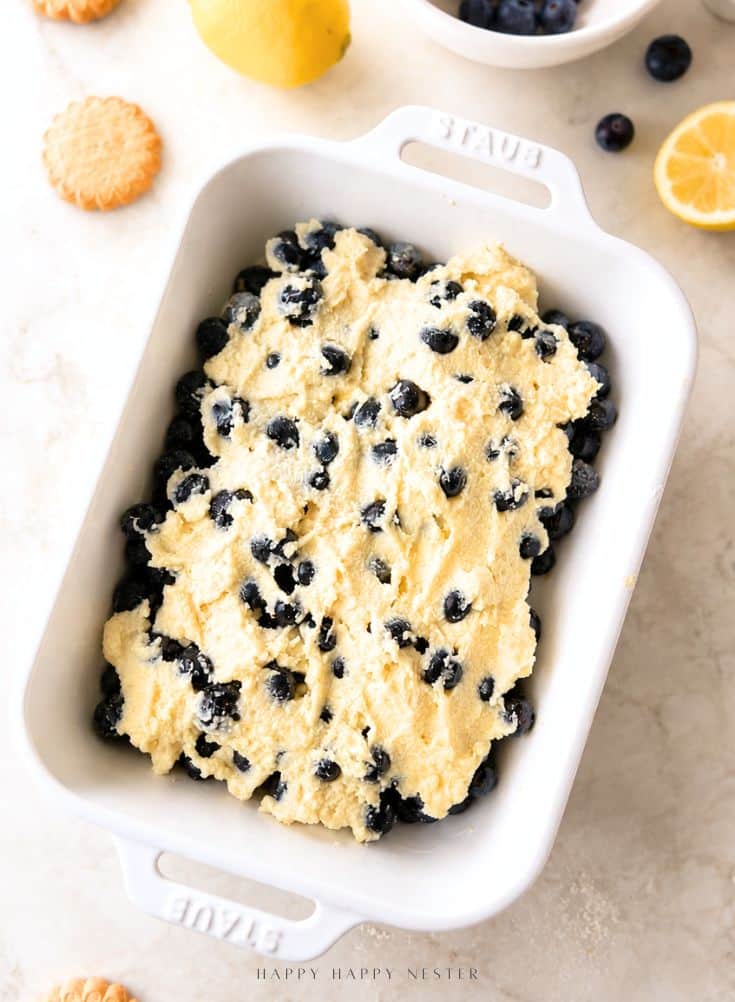 An overhead shot of the complete, unbaked Lemon Blueberry Mascarpone Crumble in the white rectangular dish, showing the texture of the shortbread-almond topping fully covering the mascarpone and blueberry layers below.