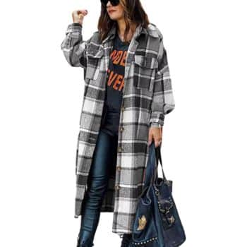 Woman wearing a long plaid coat over a black graphic t-shirt and jeans, holding a large dark handbag, and wearing sunglasses.