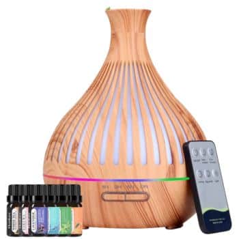 A wooden-grain essential oil diffuser with colored LED lights, a remote control, and six small bottles of essential oils are shown on a white background.