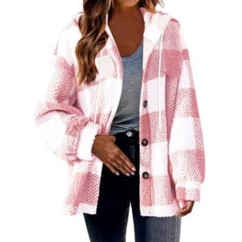 A woman wears a pink and white plaid hooded jacket over a gray shirt and black jeans. She has long, wavy brown hair and her right hand rests on her stomach.