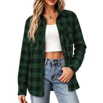 Woman wearing a green and black plaid shirt over a white crop top and light blue jeans, with long, wavy blonde hair. She stands with one hand in her pocket against a white background.