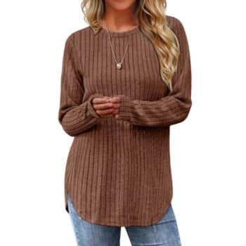 Woman wearing a long-sleeve, brown ribbed sweater with a round neckline, paired with light blue jeans and a necklace. Only her torso is visible against a white background.