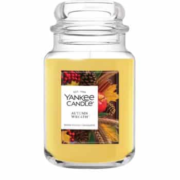 A large glass jar of Yankee Candle in the Autumn Wreath scent, featuring a yellowish-orange wax and a label with fall leaves, pinecones, and berries.