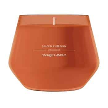 An orange Yankee Candle labeled “Spiced Pumpkin” with essential oils, shown in a wide, round glass container. The candle wick is unlit.