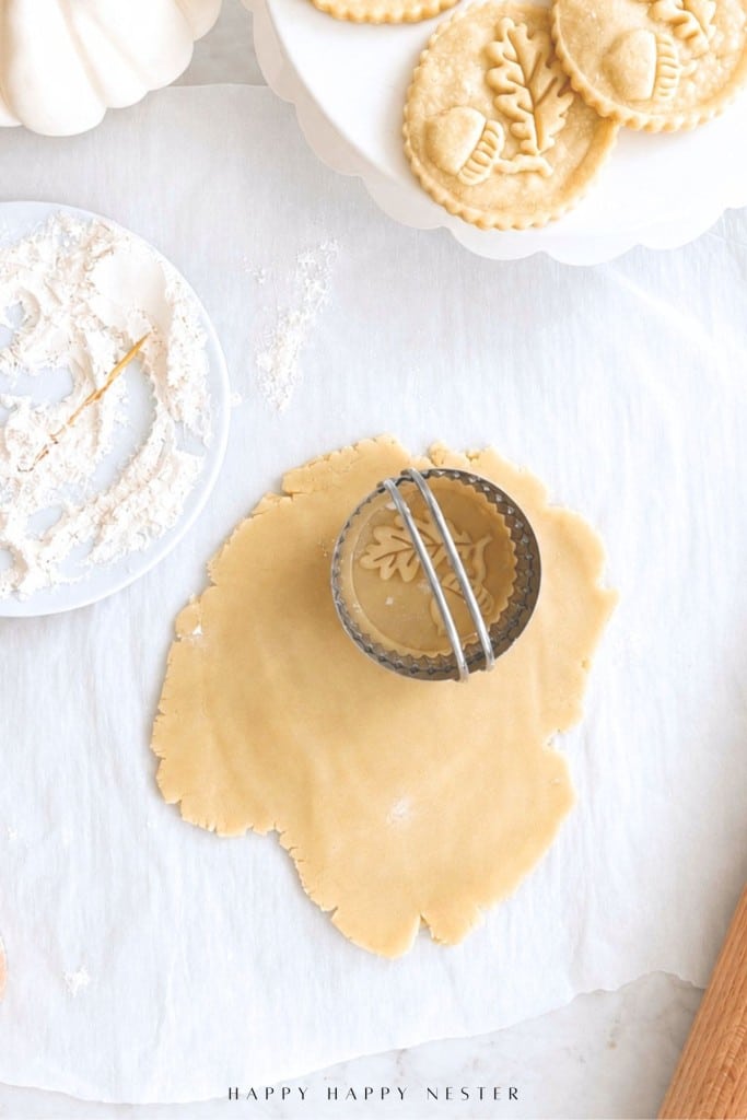 Round cookie cutter on rolled dough, with dusted flour nearby and decorated unbaked cookies on a plate at the top.