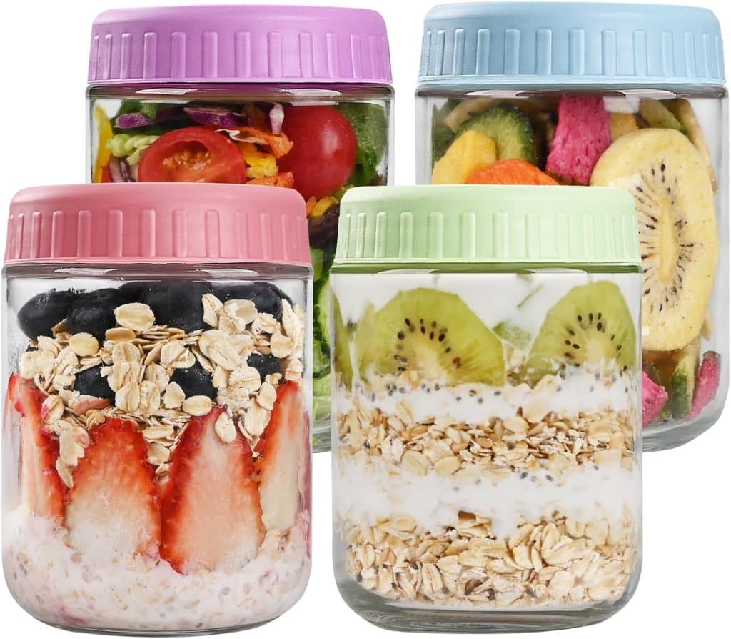 Four glass jars with pastel-colored lids, filled with assorted foods: pumpkin overnight oats topped with strawberries and blueberries, yogurt with kiwi, a garden salad, and mixed dried fruits. Each jar displays its layers through the glass.
