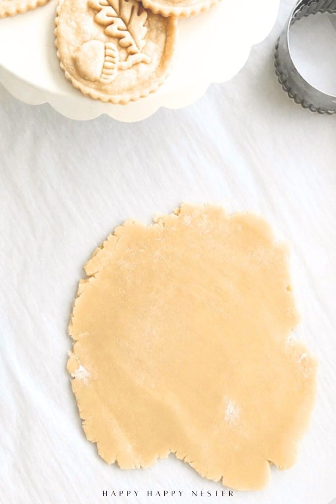 A sheet of rolled cookie dough sits on parchment paper next to a scalloped cookie cutter and a plate of stamped, unbaked cookie stamp shortbread cookies.