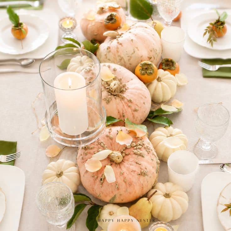 Salmon pink Cinderella pumpkins on a fall table with white mini pumpkins, persimmons, magnolia leaves, and candlelight