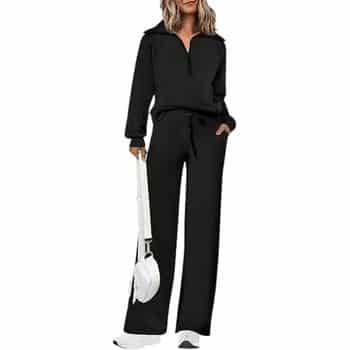 Woman in a black long-sleeve zip-up top and matching wide-leg pants, holding a white handbag, wearing white shoes.