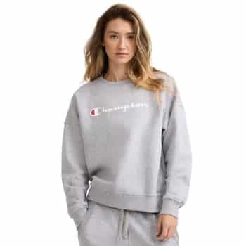 Woman wearing a gray Champion sweatshirt and matching sweatpants, standing with one hand in her pocket against a plain white background.