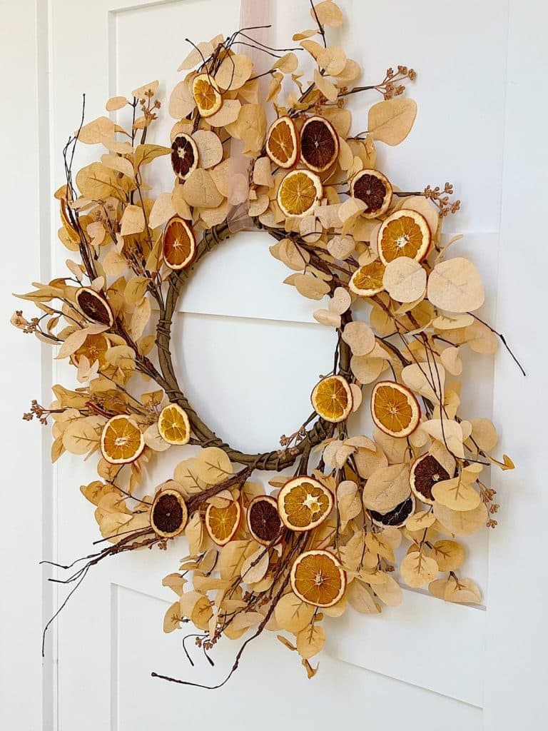 Fall wreath made with dried eucalyptus leaves, branches, and dried orange slices on a white door.
