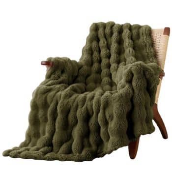 Olive green fluffy faux fur throw blanket draped over a woven accent chair in a neutral living room.
