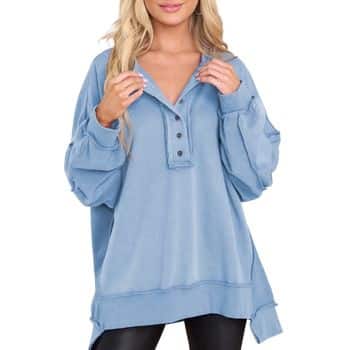 Woman wearing a loose-fitting, light blue button-up pullover sweater with long sleeves and black leggings, posing with hands near her neck. Only her upper body is visible, and her face is partially out of frame.
