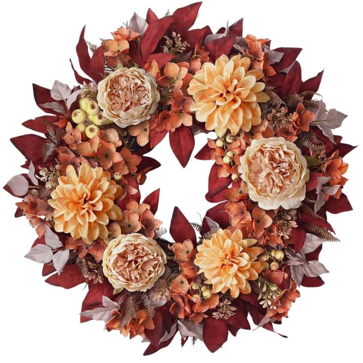 A decorative fall wreath with large cream and orange flowers, red and brown leaves, and small berries, arranged in a circle.