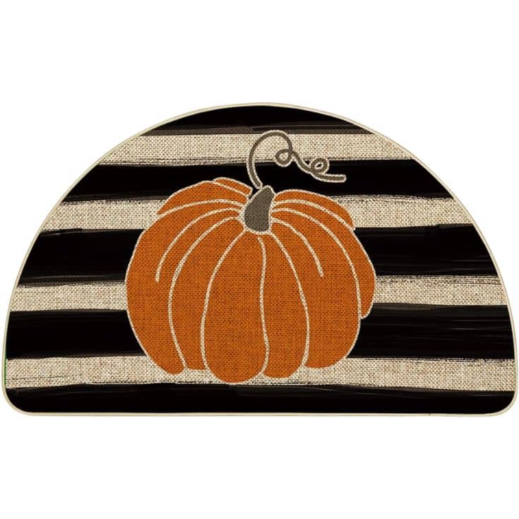 A half-circle mat with black and beige stripes, featuring an orange pumpkin with a green stem in the center.