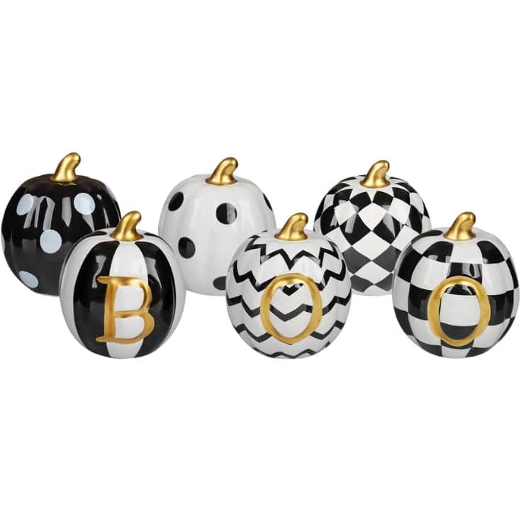 Six decorative pumpkins in black, white, and gold with various patterns and the word “BOO” spelled out on three of them, creating a festive Halloween display.
