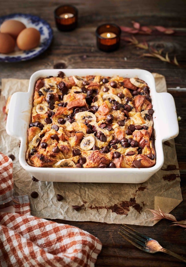 Chocolate banana bread pudding baked with sliced bananas and chocolate chips in a white baking dish.