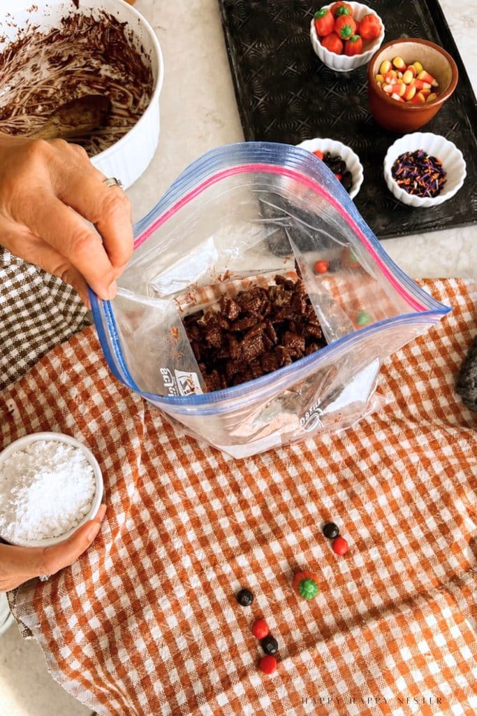 Chocolate-coated Chex in a resealable bag next to a bowl of powdered sugar ready to be added and shaken