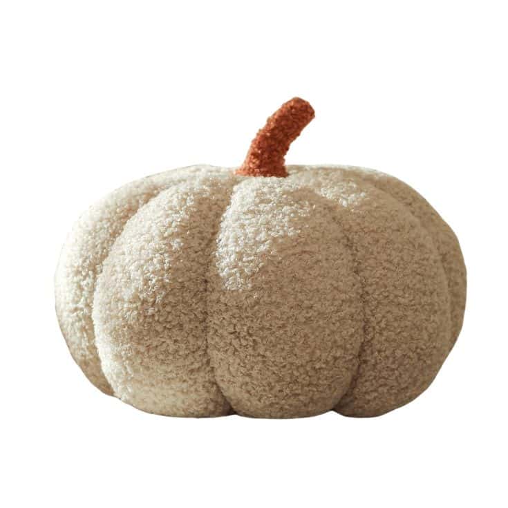 A beige, plush pumpkin-shaped pillow with a textured, fuzzy surface and a short, brown stem, set against a white background.