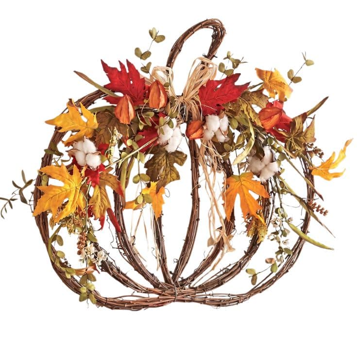 A pumpkin-shaped wreath made of brown twigs, decorated with orange, red, and yellow artificial leaves, white cotton, and raffia, set against a white background.