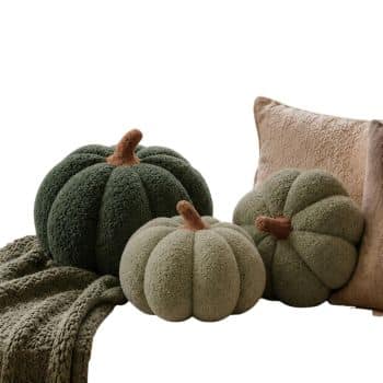 Dark green and sage sherpa pumpkins styled on a neutral sofa with a textured throw and pillows for fall.