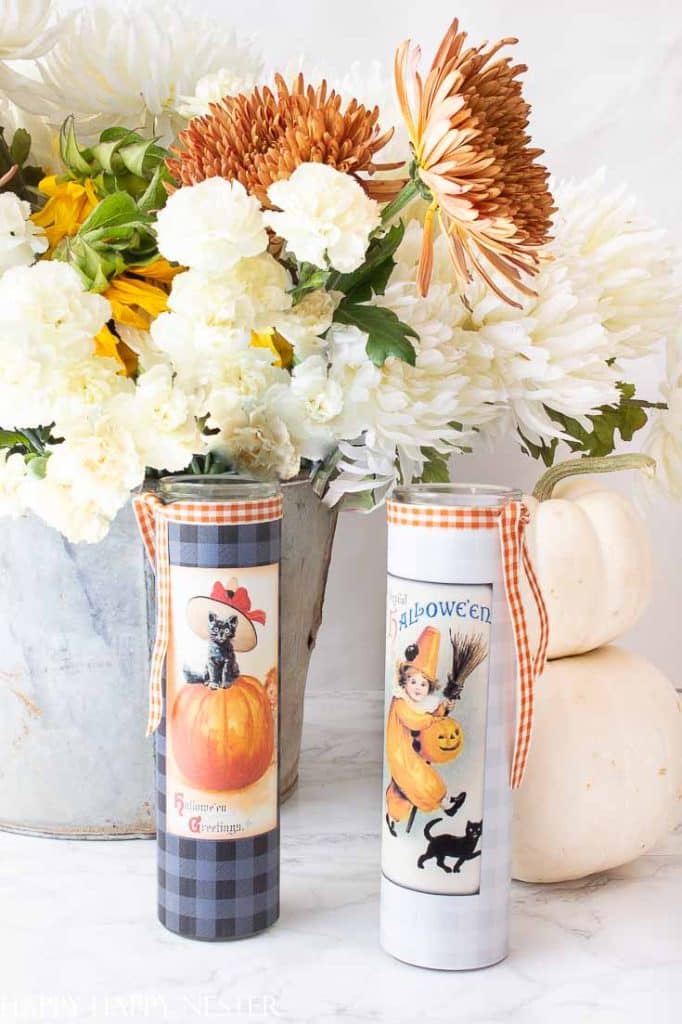 Halloween candles decorated with vintage printable labels, plaid paper, and orange gingham ribbon beside white pumpkins.