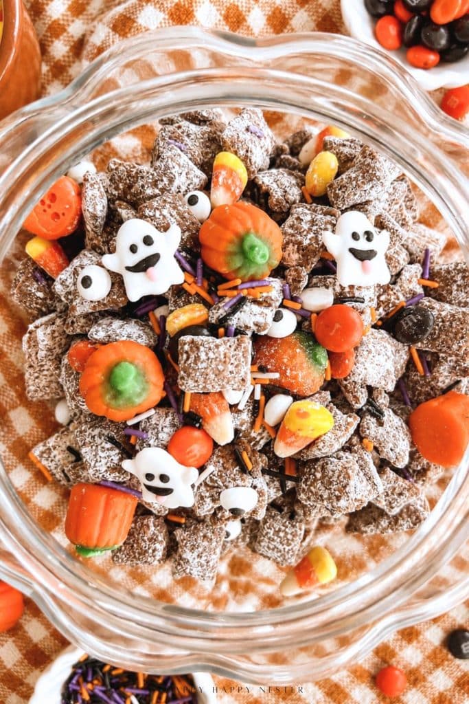 Close-up of Halloween puppy chow with candy eyeballs and orange and black M&M's in a glass pumpkin jar