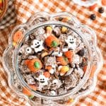 Overhead view of an open glass pumpkin cookie jar filled with Halloween puppy chow, candies, and candy ghosts