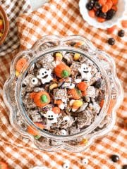 Overhead view of an open glass pumpkin cookie jar filled with Halloween puppy chow, candies, and candy ghosts