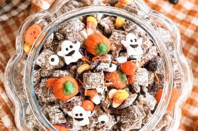 Overhead view of an open glass pumpkin cookie jar filled with Halloween puppy chow, candies, and candy ghosts