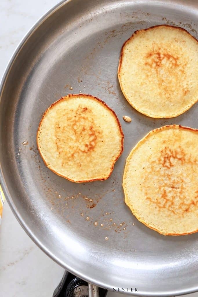 Three thin golden brown homemade pancakes cooking together in a large skillet
