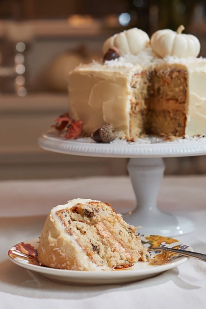 Layered Italian cream cake with pumpkin filling, cream cheese frosting, coconut, and white pumpkin decorations.