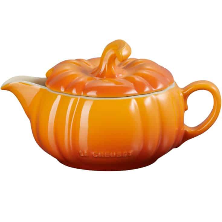 Orange pumpkin-shaped teapot with a handle and spout, featuring a lid shaped like a pumpkin stem. The teapot has a glossy finish and the brand name “Le Creuset” is visible on the side.