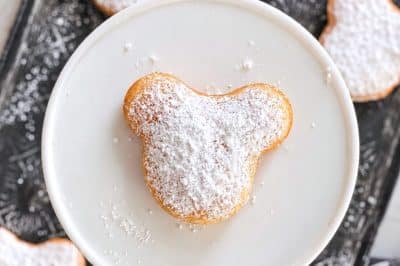 Mickey-shaped beignets generously dusted with powdered sugar after frying