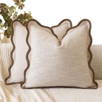 Neutral linen-look throw pillows with contrasting brown scalloped trim on a cream sofa.