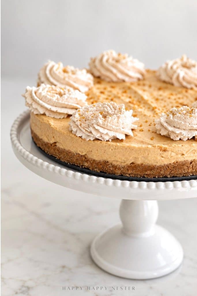No bake pumpkin cheesecake with a graham cracker crust and cinnamon whipped cream topping on a white cake stand.