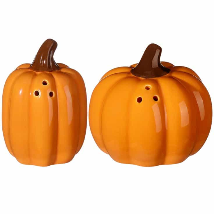 Two ceramic pumpkin-shaped shakers with brown stems, each having holes on top, placed side by side on a white background.