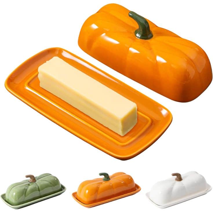 Ceramic butter dishes shaped like pumpkins in orange, green, and white, with matching bases. The orange dish is open, showing a stick of butter on the base.